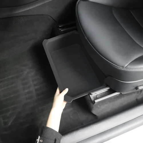 Person pulls out a shallow black plastic storage tray from beneath a car seat inside a vehicle, showing an interior organizer.