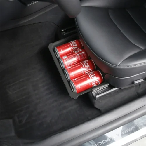 Coca‑Cola cans stored in a small tray under a car seat in a dark interior.