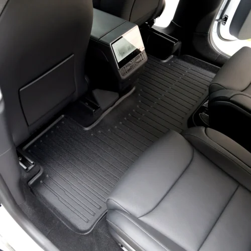 Rear passenger area of a car with black leather seats, a center console touchscreen, and ribbed rubber floor mats