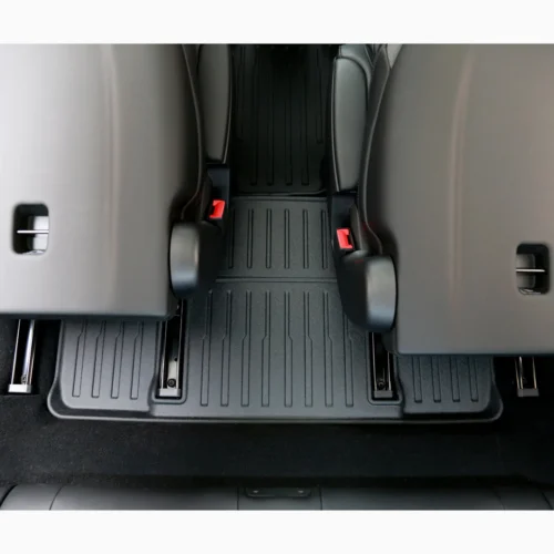 View of a car's rear passenger area with two folded seats, black ribbed floor mats, and red seat belt buckles visible between the seats.