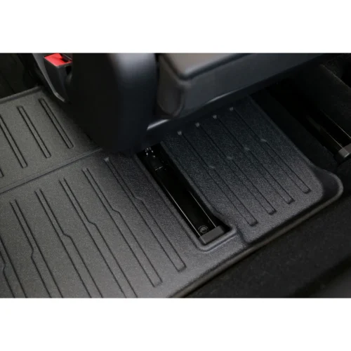 Close-up of a car floor mat with textured grooves and a central slot where the mat anchors to the floor rail, near the driver's seat.