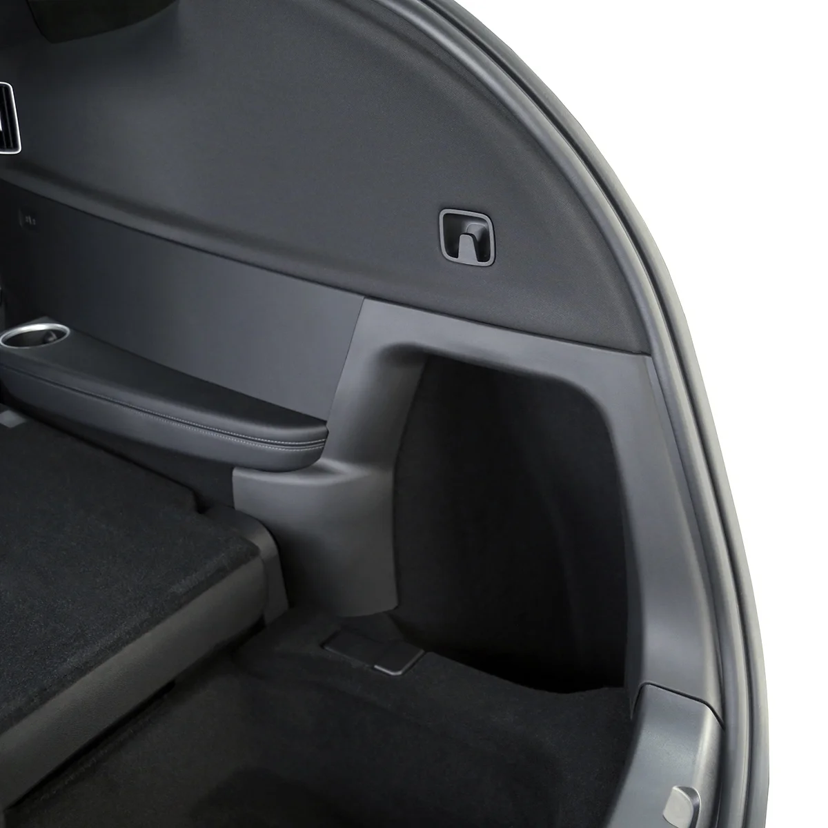 Close-up of a car's rear cargo area: side panel with a small square latch, black upholstery, and a cup holder along the edge.