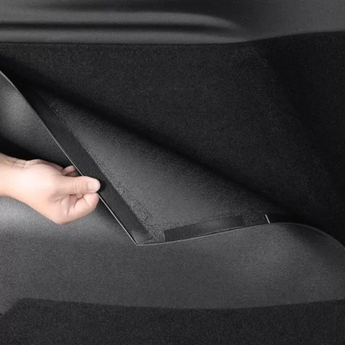 Person lifting a floor panel inside a car to reveal a storage compartment beneath the rear seat.
