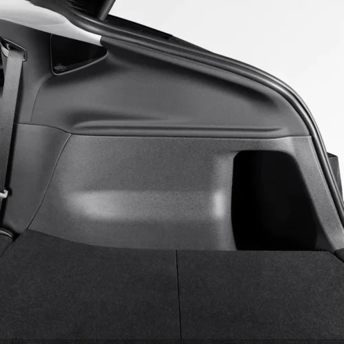 Interior of a car trunk showing a grey side panel and dark cargo floor, with folded rear seat behind.