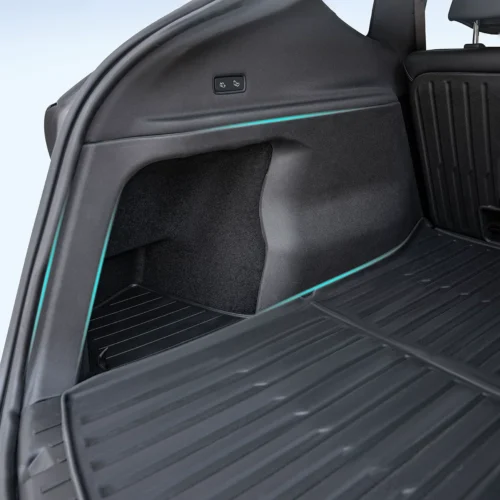 Car trunk area showing side storage panel, cargo mat, and a small control panel for rear-seat functions on the side wall.