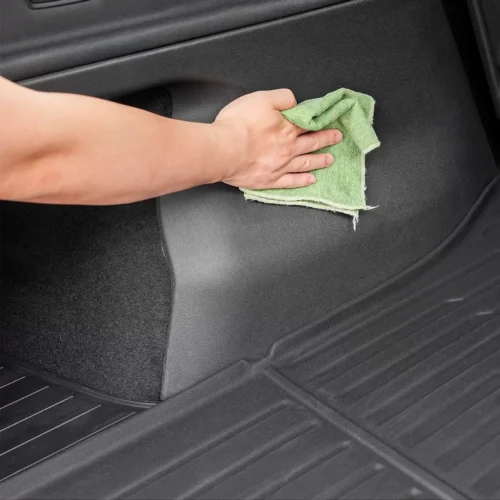 Person's hand wiping the car's floor panel with a green cloth.