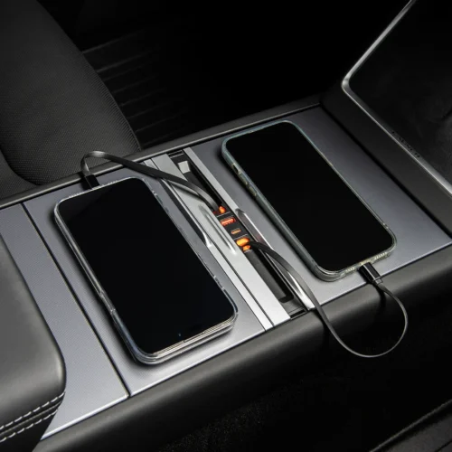 Two smartphones sit on a car's center console charging dock, connected by USB cables with orange charging indicators glowing in the slot panel