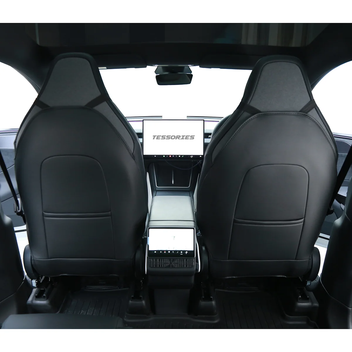 Rear-view inside a modern car: two black leather front seats with high backs, center console, and a dashboard screen showing 'TESSORIES'.