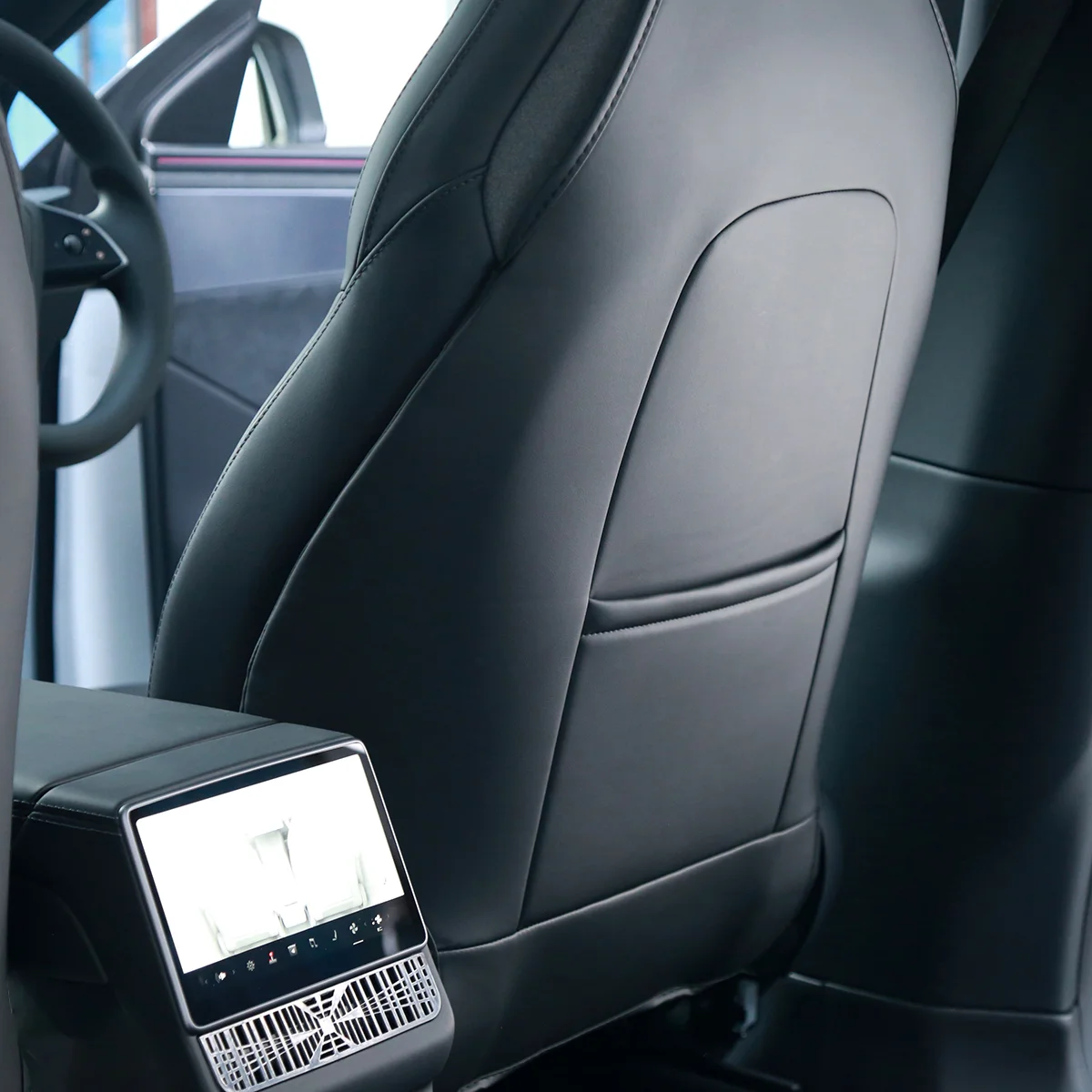 Rear view of a modern car interior: back of the front seat with a mounted touchscreen console and visible air vents below it