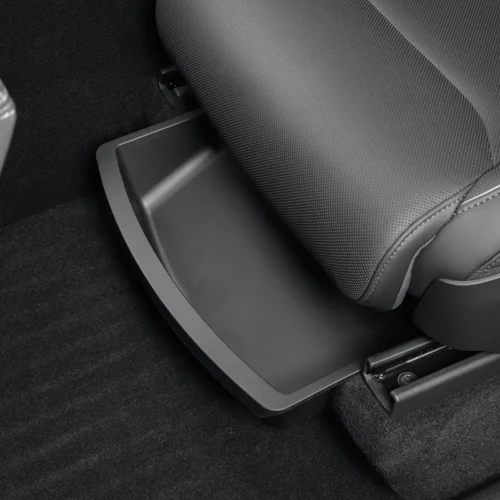Plastic storage tray tucked under a car seat on a dark carpeted floor, showing a knee-level compartment design.