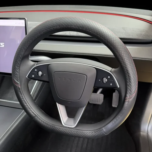 Tesla steering wheel with textured grip and red stitching, multifunction controls on both sides, and a centered TESLA badge; pedals visible below.