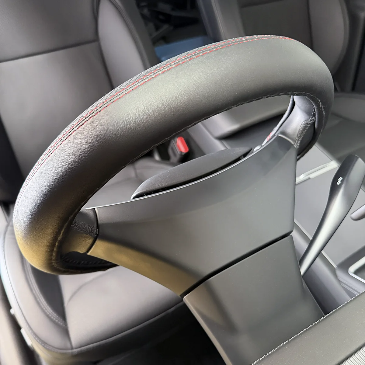 Close-up of a car steering wheel with red contrast stitching on black leather, showing grip and spokes inside the cabin