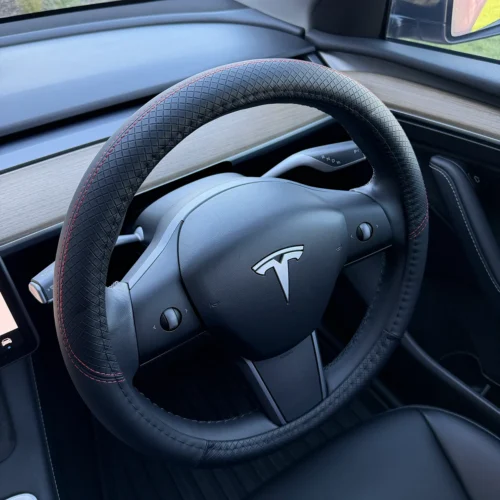 Tesla steering wheel with black perforated grip and red stitching in a sleek car interior.