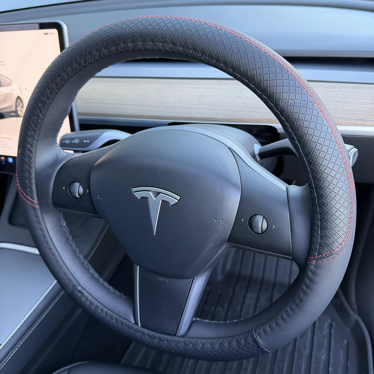 Close-up of a Tesla steering wheel with a diamond-pattern grip and red stitching inside a car interior