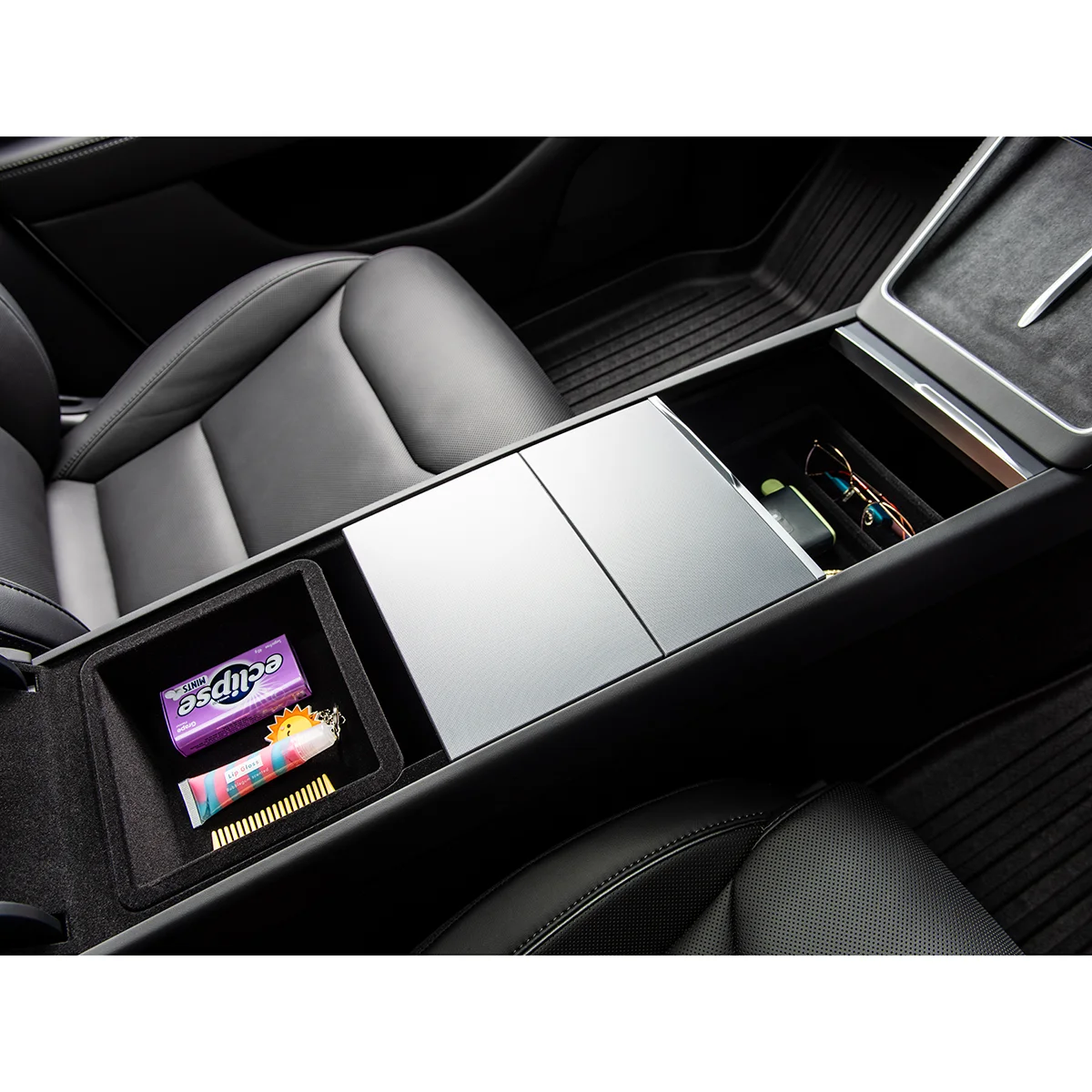 Luxurious car interior focusing on the center console with an open storage tray showing sunglasses and small items inside, beside leather seats.