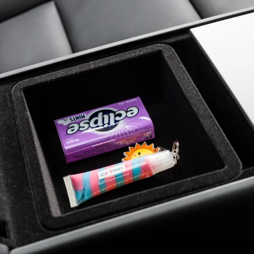 Open car console tray showing a purple-wrapped chocolate bar and a colorful striped lip gloss tube with a sun-shaped keychain accessory nearby.