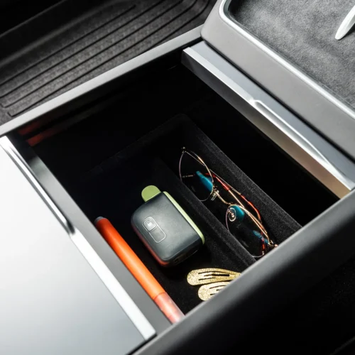 Open car center console drawer with sunglasses, a key fob, an orange pen, and gold hair clips in view.