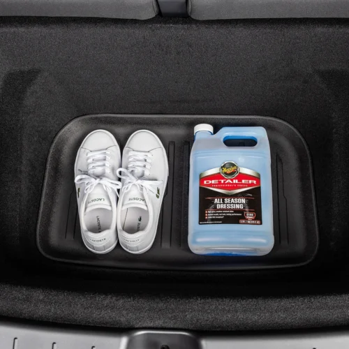Pair of white Lacoste sneakers and a blue jug of Meguiar's All Season Dressing stored in a car trunk tray.