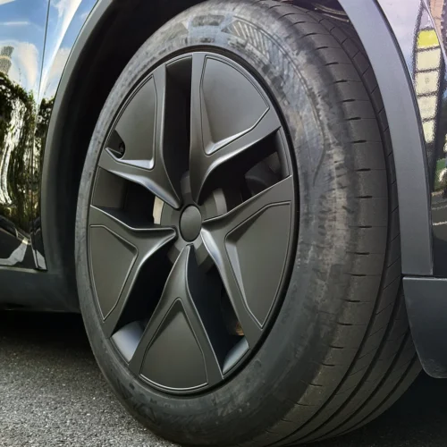 Close-up of a car wheel with a dark gray, star-shaped alloy rim and low-profile tire near the car body surface.