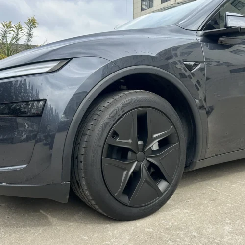 Front left wheel and fender of a dark gray car, featuring a black aero wheel cover and surrounding bodywork; part of the headlight and mirror visible on top edge.