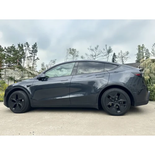 Side view of a dark gray electric SUV parked on a concrete driveway with trees in the background.