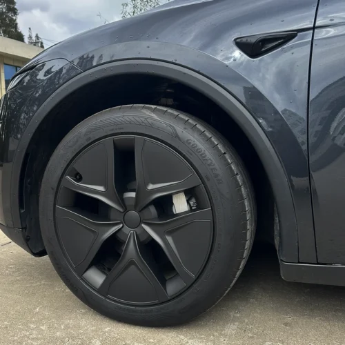 Close-up of a dark gray car's front wheel with an aerodynamic composite rim and Goodyear tire, showing the fender and door seam above it.