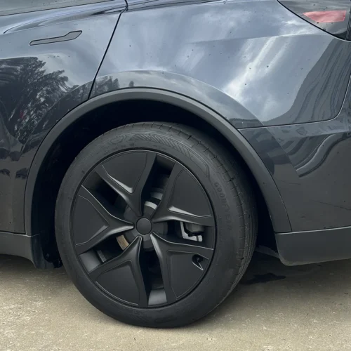 Close-up of a dark car's front left wheel with a five-spoke matte black alloy rim and a Goodyear tire.