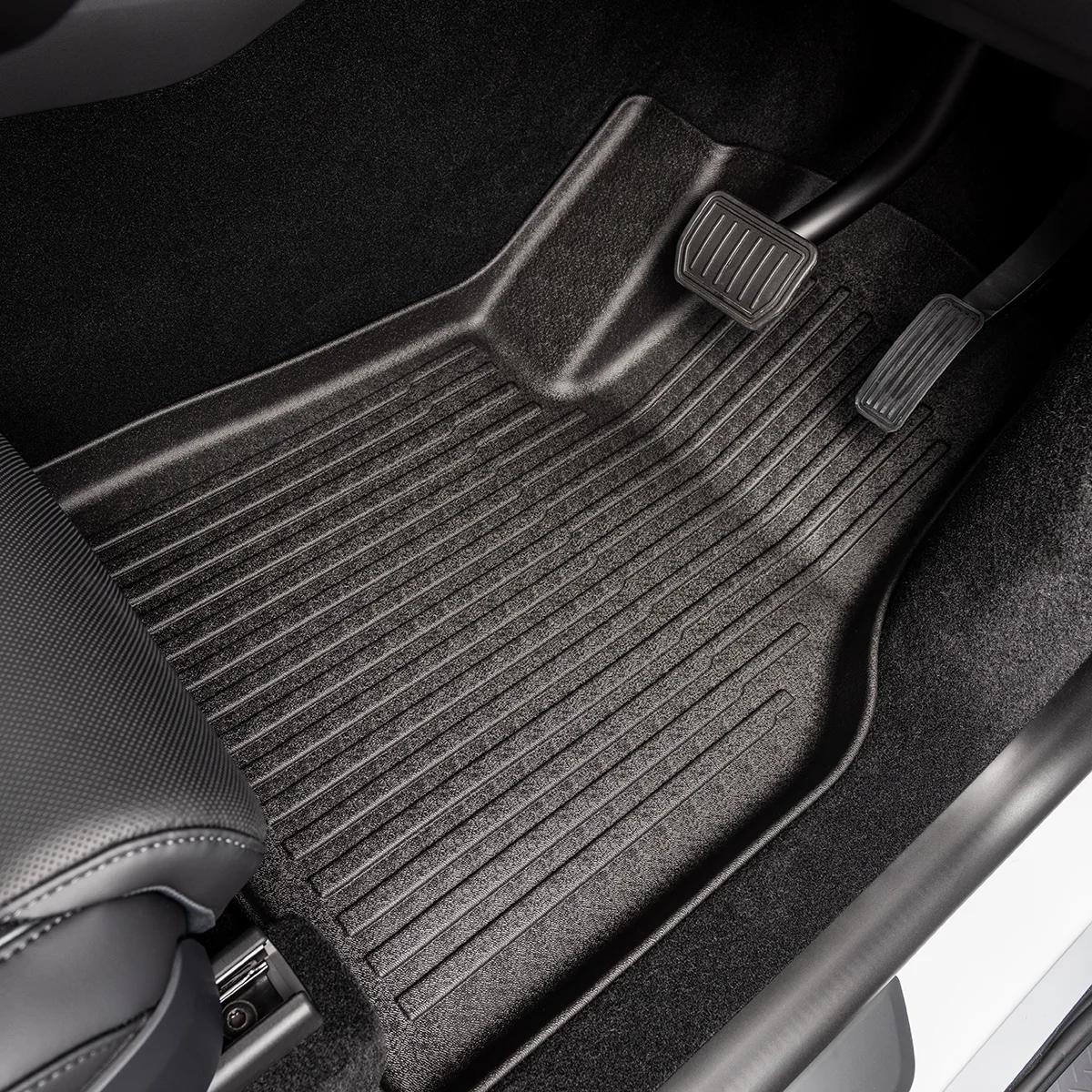 Driver's footwell with a textured rubber floor mat and two pedals (brake on left, accelerator on right).