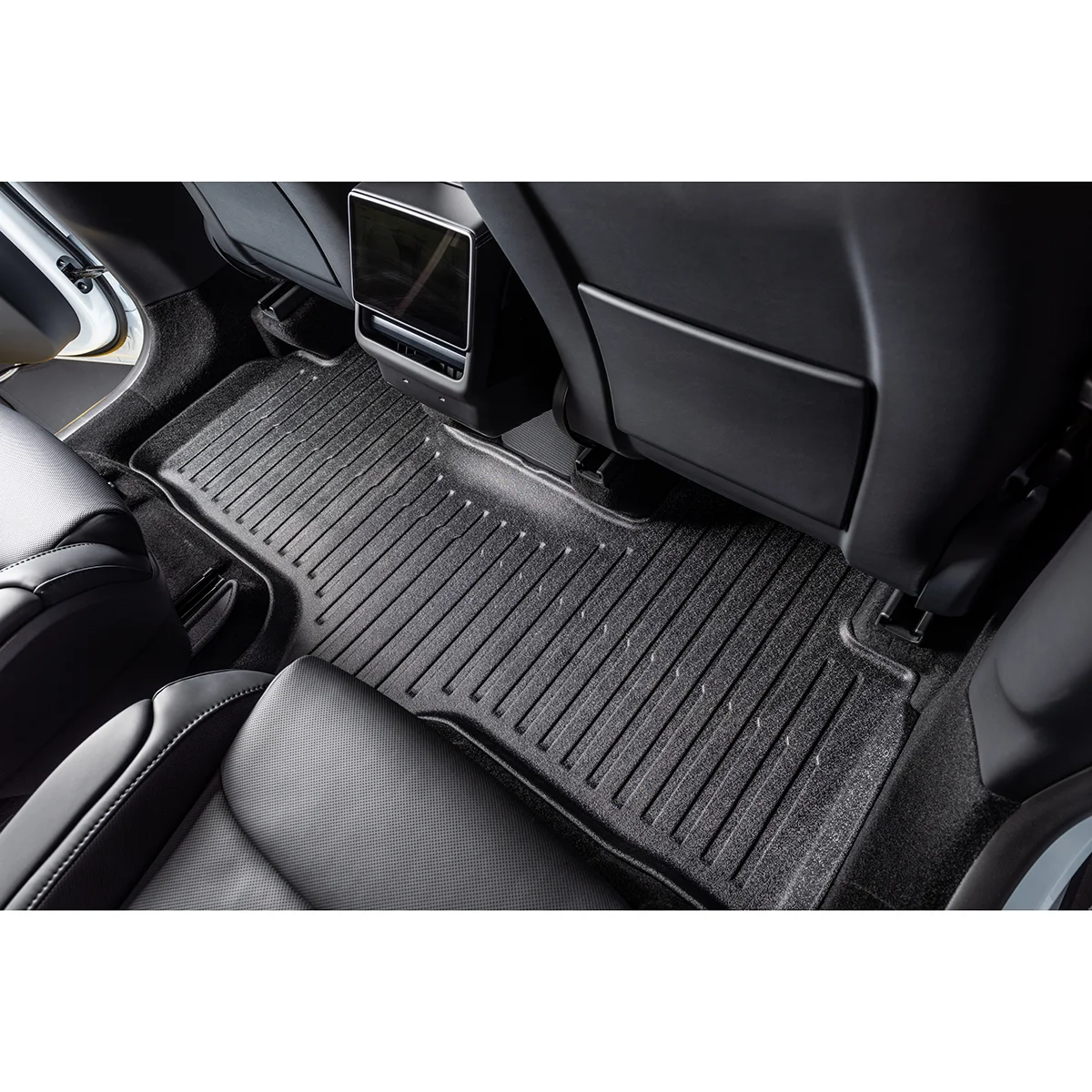 Back seat area of a car with a ribbed rubber floor mat and a center console screen between the front seats.