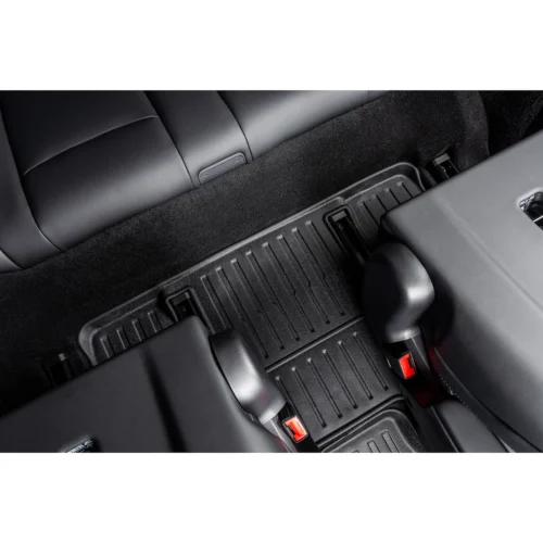 Back seat area of a car with a textured rubber floor mat and red seat belt buckles visible in the foreground.