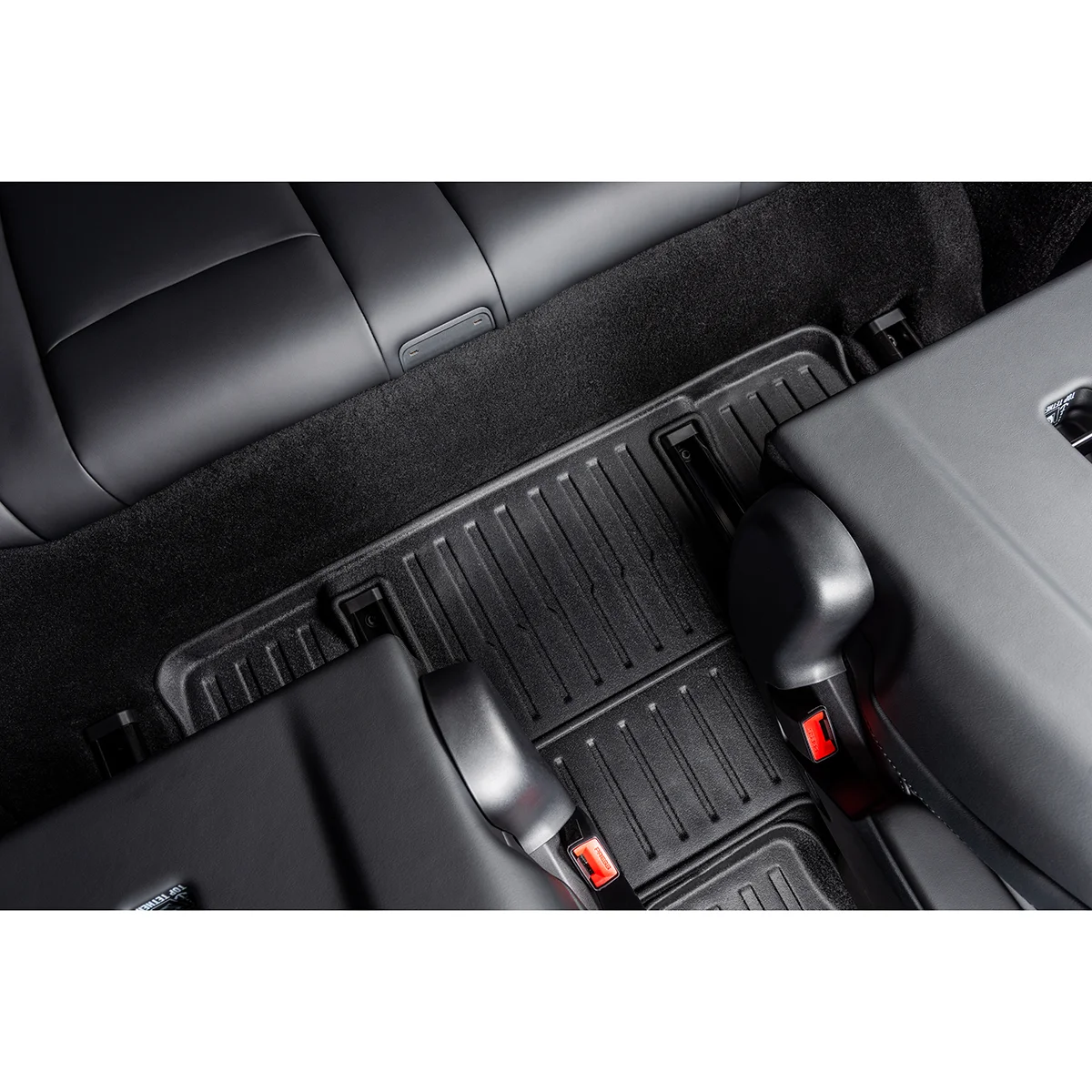 Back seat area of a car with a textured rubber floor mat and red seat belt buckles visible in the foreground.