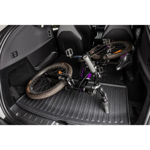 Mountain bike laying in the back of an SUV, with muddy tires and pedals visible on a rubber cargo mat inside the trunk