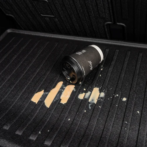 Black McCafé coffee cup lying on a textured truck bed liner with spilled beige coffee beside it.