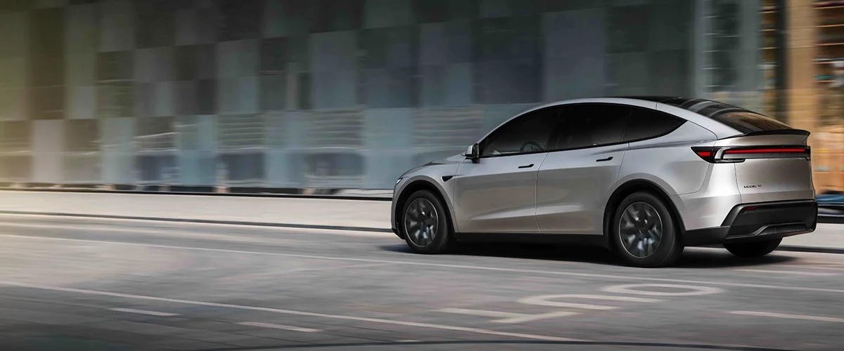 Silver SUV in motion on an urban street beside a glass-fronted building.
